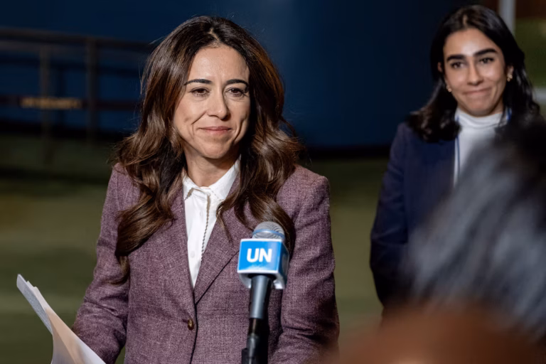 A woman in a purple blazer speaks into a UN microphone while holding papers