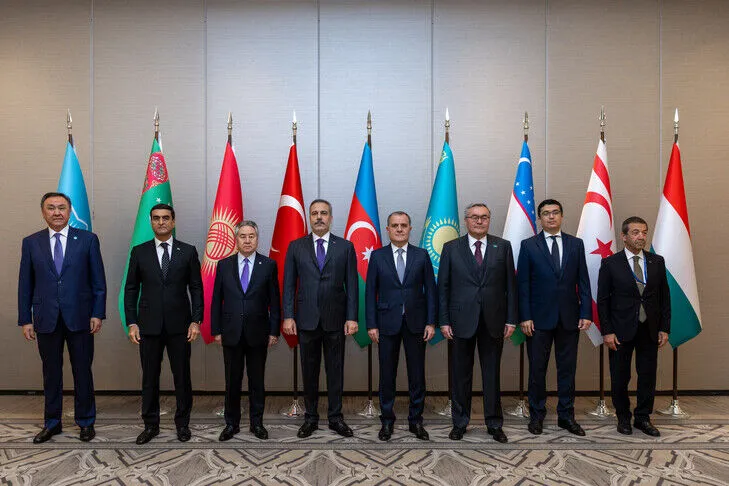 Eight diplomats standing in a row in front of national flags during an official summit