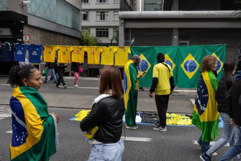 People wrapped in Brazilian flags walk past street vendors displaying national soccer team jerseys and flags
