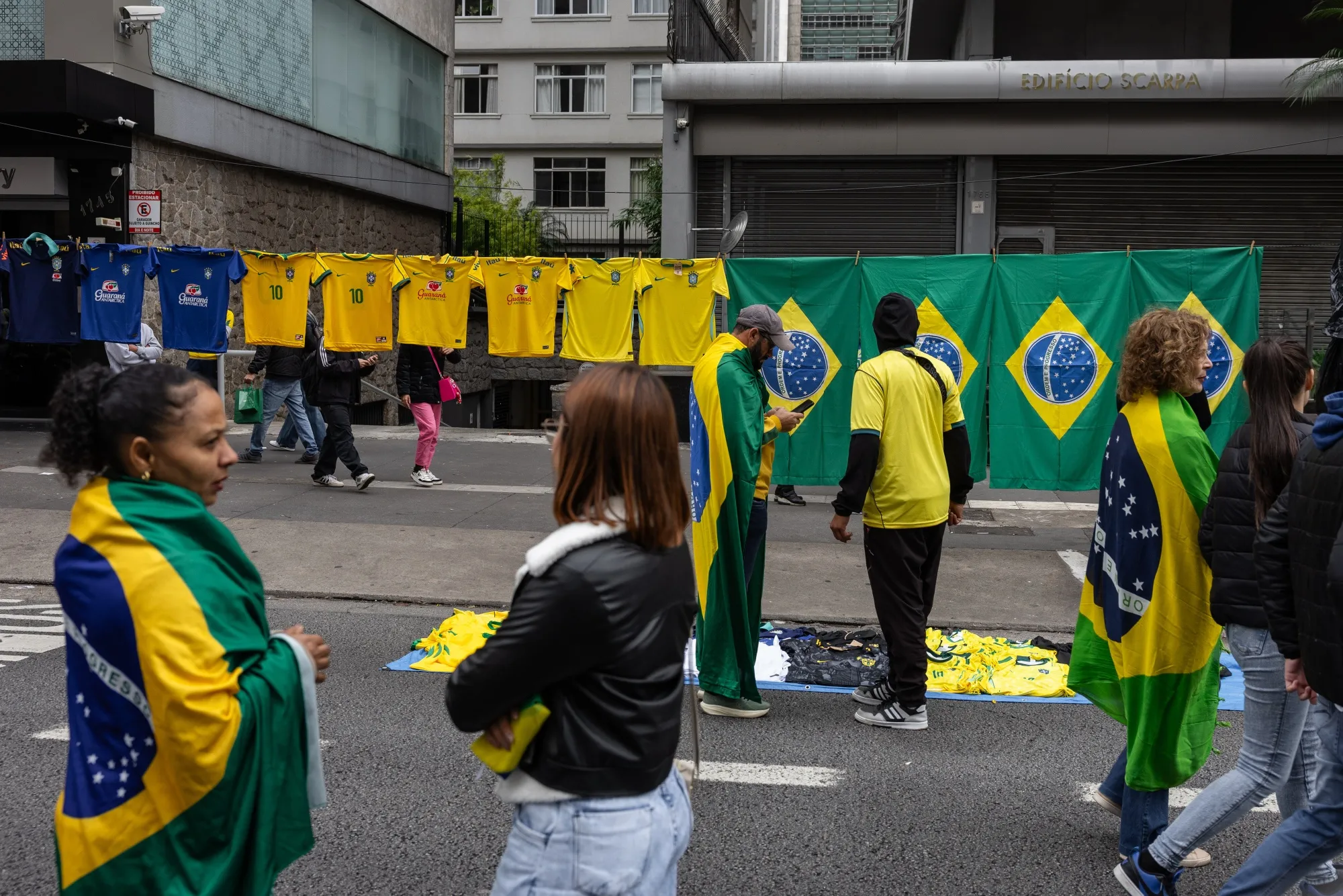 People wrapped in Brazilian flags walk past street vendors displaying national soccer team jerseys and flags