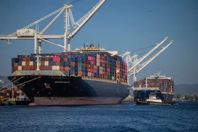 Large container ship Seaspan Bravo loaded with shipping containers docked at a port under giant cranes