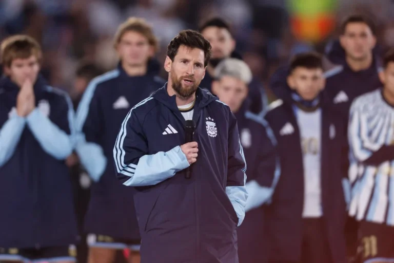 Lionel Messi speaking into a microphone in an Argentina team jacket with his teammates standing behind him