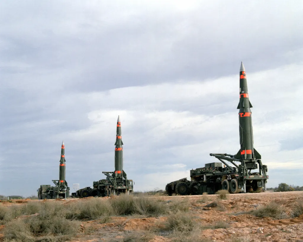 Three military ballistic missiles raised vertically on mobile launcher vehicles in an open field