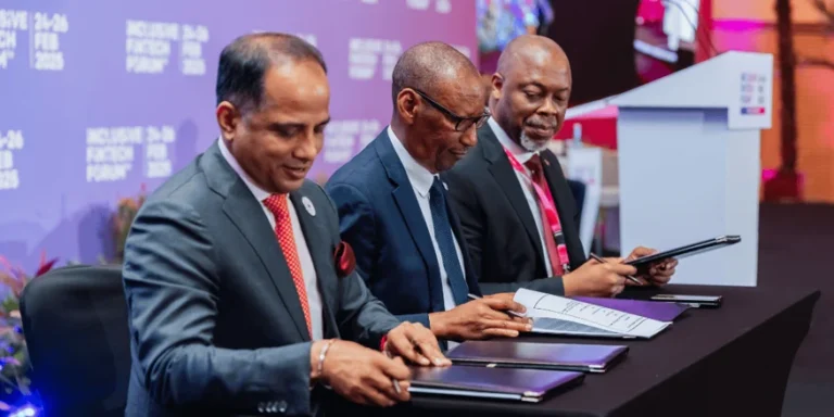 Three men in suits seated at a table signing documents at the Inclusive FinTech Forum