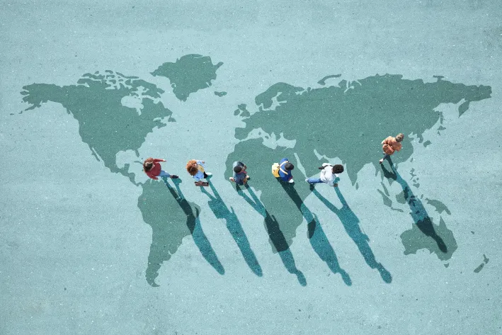 Top-down view of people walking in a line across a large world map painted on the pavement