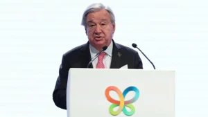 António Guterres speaking into microphones at a white podium with a colorful butterfly logo