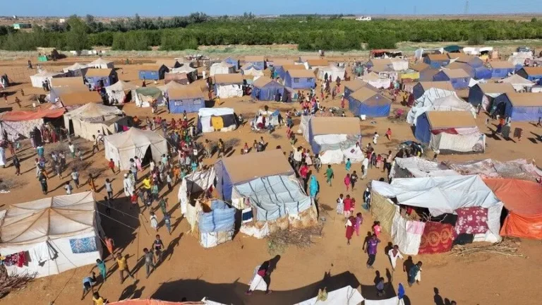 Aerial view of a crowded settlement of makeshift tents and tarp shelters on dry, sandy ground