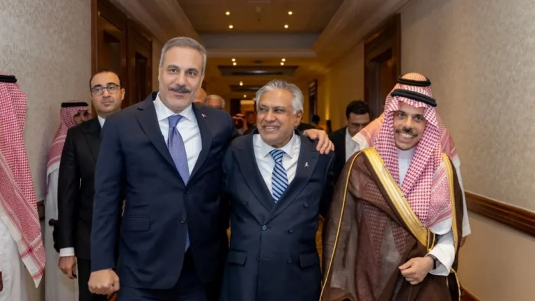 Turkish Foreign Minister Hakan Fidan, Pakistan Foreign Minister Ishaq Dar, and Saudi Foreign Minister Prince Faisal bin Farhan smile while walking together in a hallway