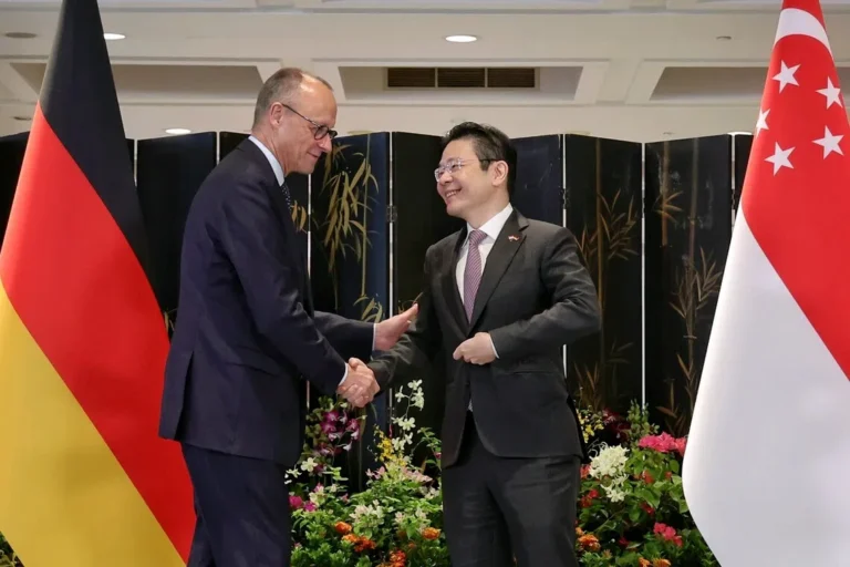 Friedrich Merz shaking hands with Singapore Prime Minister Lawrence Wong between the German and Singapore flags