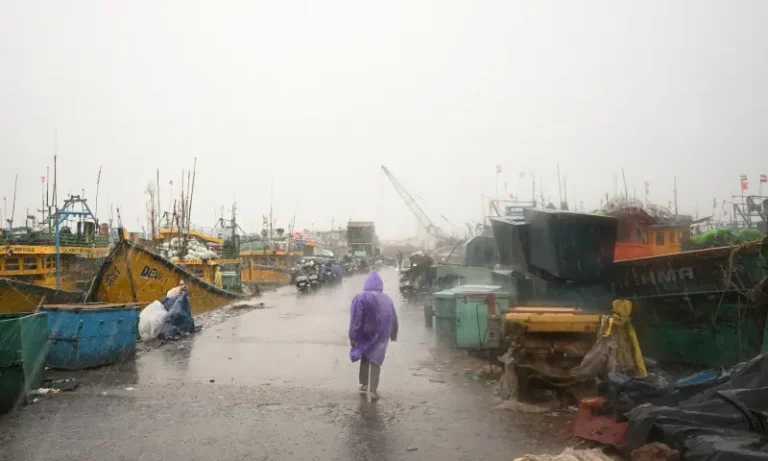 A person in a purple raincoat walks down a wet harbor pier lined with docked fishing boats during heavy rain