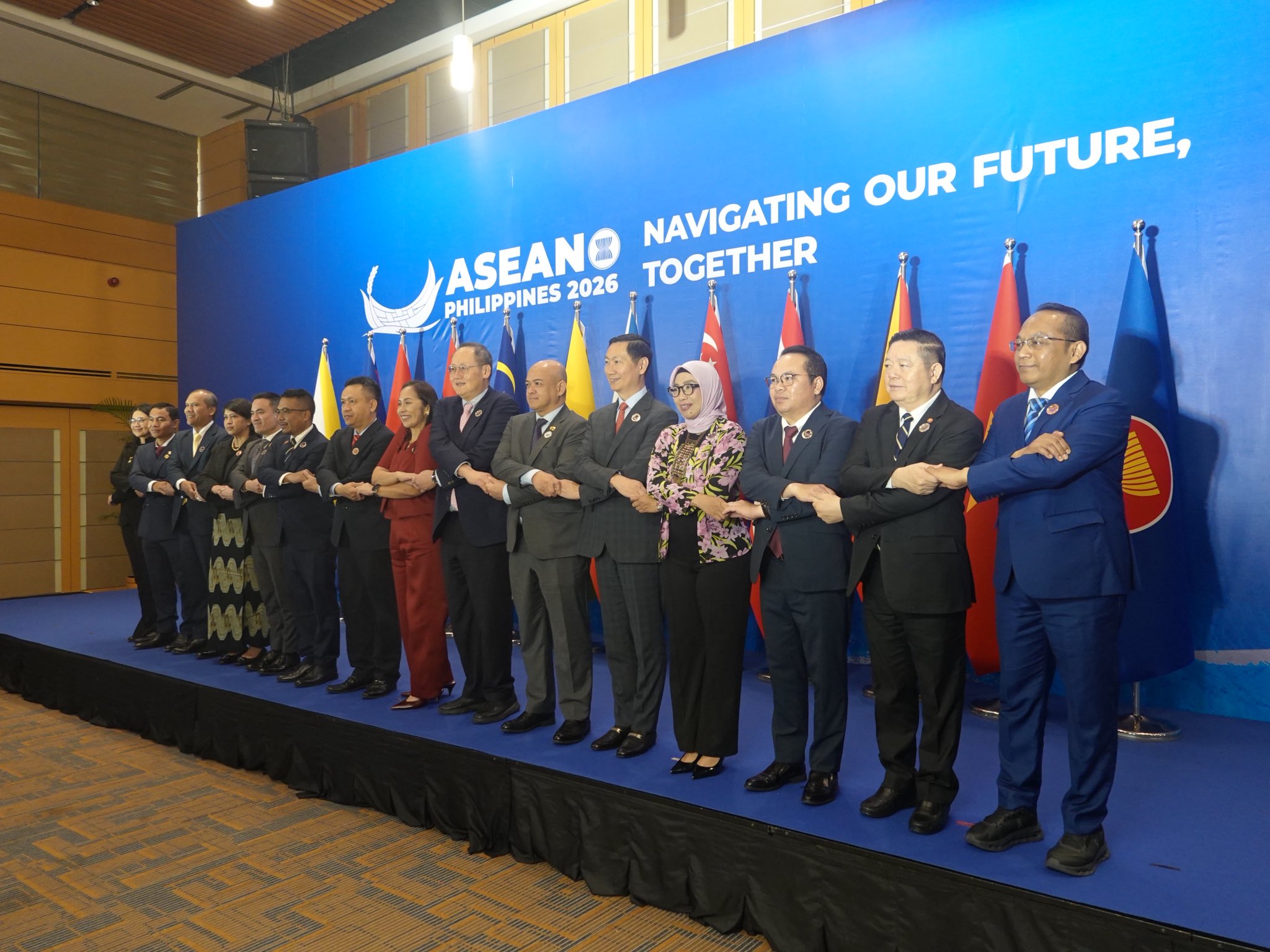 Delegates perform the ASEAN cross-arm handshake in front of a backdrop reading ASEAN Philippines 2026