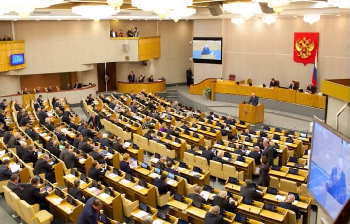 A plenary session in the Russian State Duma with delegates seated at rows of desks and a speaker at the podium