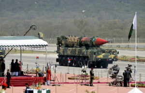 Pakistani military vehicle carrying a large camouflage missile during a parade with soldiers standing atop the launcher