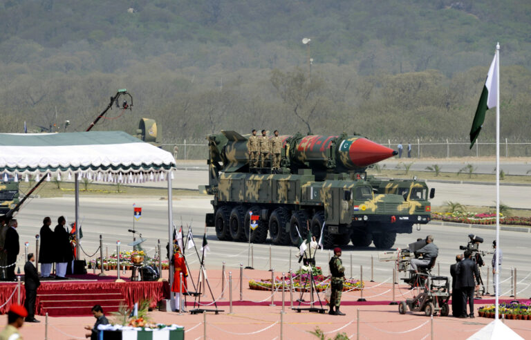 Pakistani military vehicle carrying a large camouflage missile during a parade with soldiers standing atop the launcher