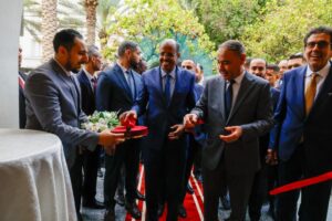Officials in suits participate in a red ribbon cutting ceremony outdoors