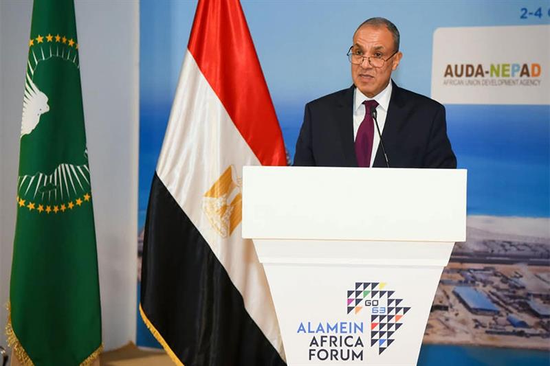 A man in a suit speaks at a podium with the Alamein Africa Forum logo, flanked by the Egyptian and African Union flags