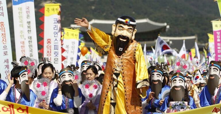 A mascot dressed as legendary founder Dangun waves at a festival alongside participants holding matching masks