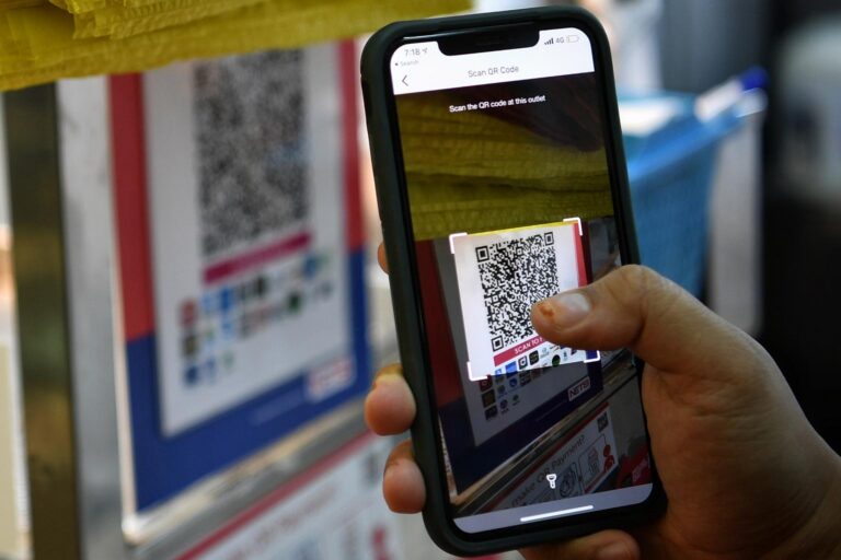 A hand holding a smartphone to scan a printed QR code for payment