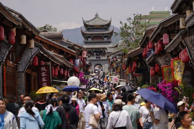 Crowded street lined with traditional Chinese buildings and lanterns leading toward a multi-tiered gate tower