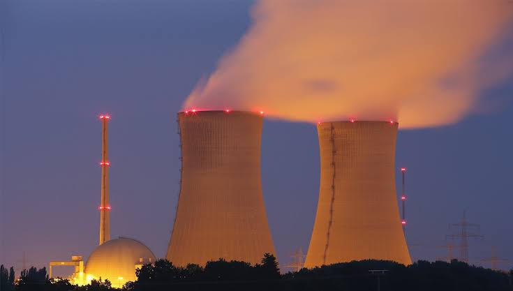 Nuclear power plant cooling towers emitting steam illuminated against a dusk sky