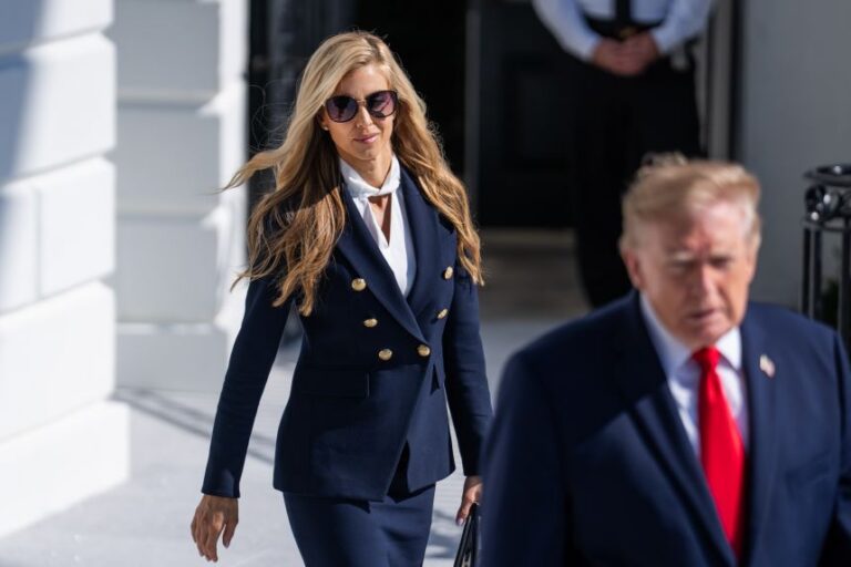 Alina Habba wearing sunglasses and a navy suit walking behind Donald Trump outdoors