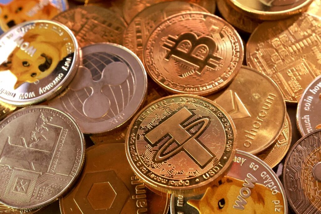 A pile of physical cryptocurrency coins, including Bitcoin, Tether, Ethereum, XRP, and Dogecoin