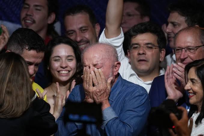 Luiz Inácio Lula da Silva covers his face with both hands in emotion while surrounded by smiling supporters