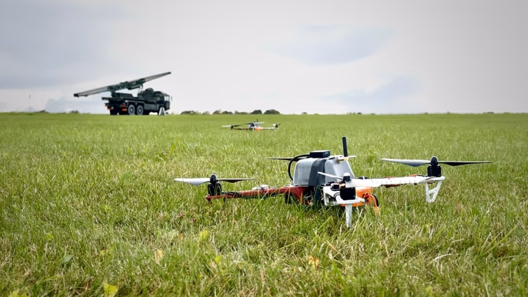 Quadcopter drone in a grassy field with a military radar truck parked in the background