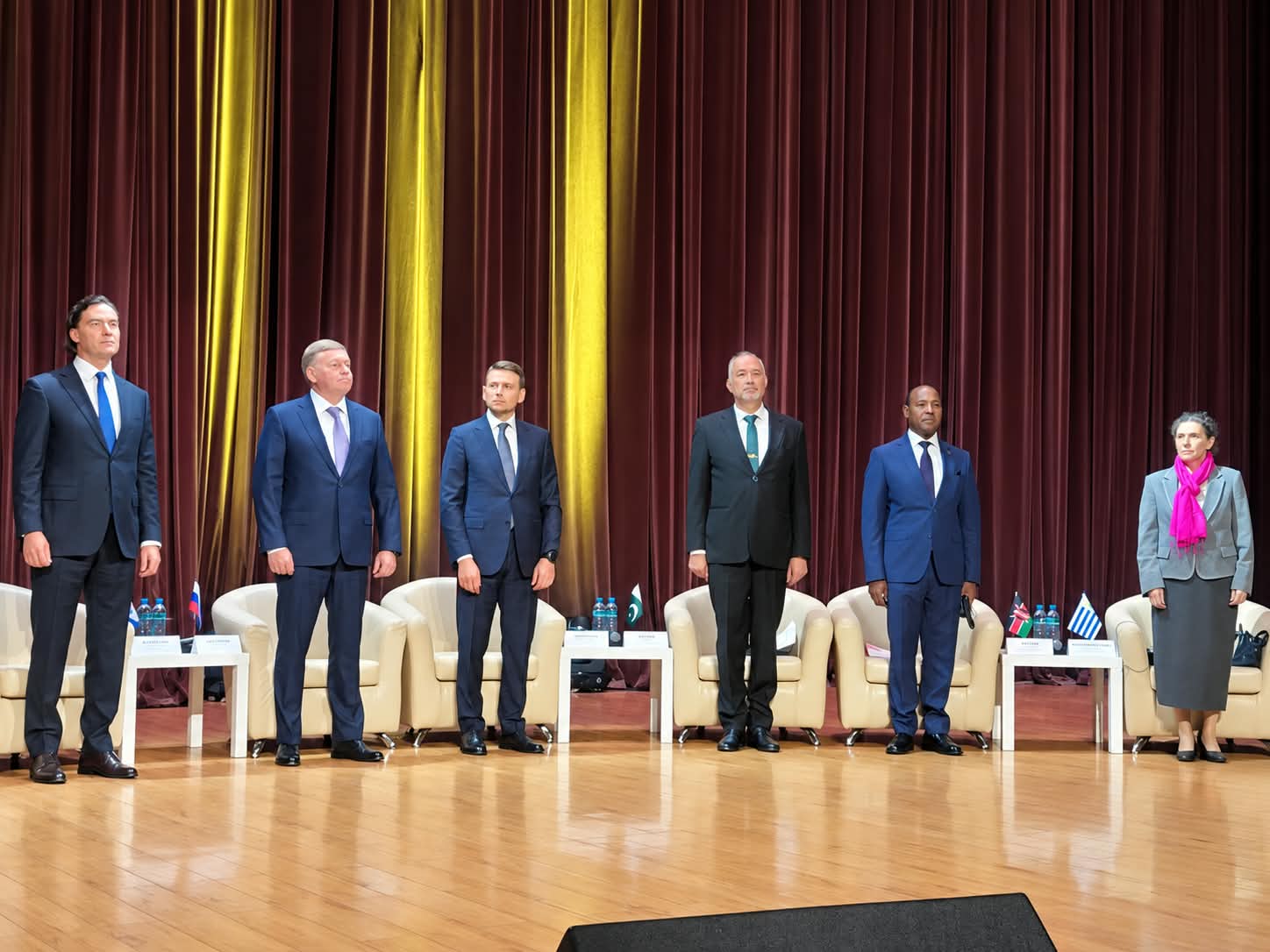 Six international delegates standing in a line on a stage during an official conference