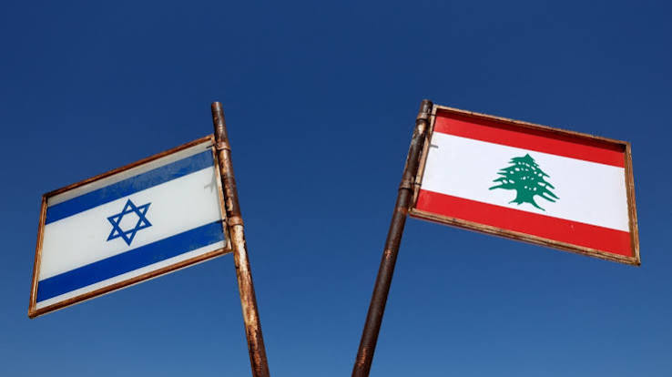 Flags of Israel and Lebanon mounted on metal poles against a clear blue sky