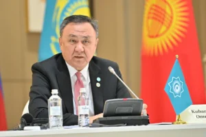 Kubanychbek Omuraliev speaking at a diplomatic meeting with flags in the background