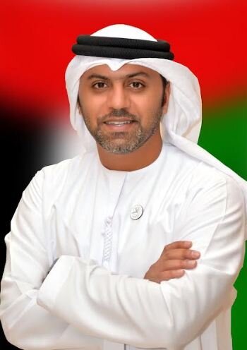 UAE Ambassador to Pakistan, Hamad Obaid Alzaabi, wearing traditional Emirati attire with a kandura and ghutra, standing in front of a background of the UAE flag.
